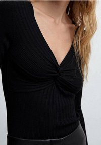 Schwarzes, geripptes Langarmshirt mit tiefem V-Ausschnitt und gedrehtem Vorderteil. Der Stoff hat eine glatte Textur und eine eng anliegende Passform.