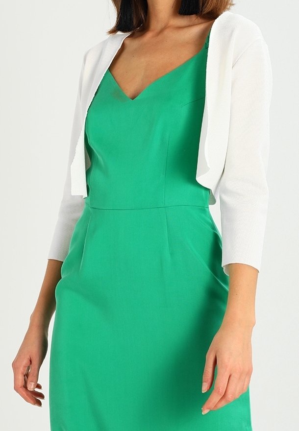 Zelené šaty bez rukávů s výstřihem do V a přiléhavým střihem, doplněné bílým krátkým kardiganem s tříčtvrtečními rukávy.