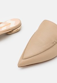 Mules beige en cuir à bout pointu, à enfiler, avec talons plats bas, présentant un matériau texturé et des détails cousus.