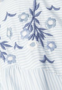 Tessuto a righe blu chiaro con ricami floreali intricatissimi in varie tonalità di blu e bianco, con dettagli a foglia e texture arricciata.