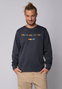 Dunkelblauer Sweatshirt mit gerippten Bündchen und Saum. Mit mehrfarbigem Text "SPREAD LOVE NOT HATE" und Herzsymbolen in verschiedenen Farben.