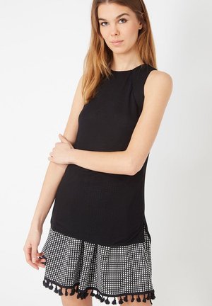 Top sin mangas negro con un diseño texturizado, combinado con una falda de cuadros en blanco y negro con un dobladillo con volantes y detalles de borlas.