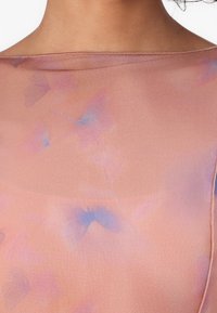 Sheer, soft fabric top in a light peach color, featuring a subtle butterfly pattern in pink and blue hues; smooth texture and boat neckline.