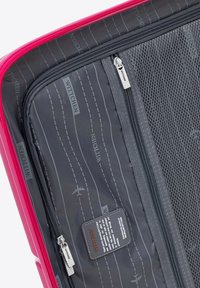 Interno di una valigia rosa con foderatura grigia, testo stampato e motivi di aerei, scomparti con zip e un'etichetta con il marchio.