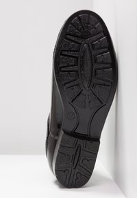 Semelle de chaussure noire avec des crampons profonds et structurés et le numéro de pointure 37 embossé près du talon, photographiée sur un fond blanc.