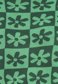 Knitted green fabric featuring a checkered pattern with dark green flowers. Texture appears soft, with distinct flower shapes and contrasting colors.