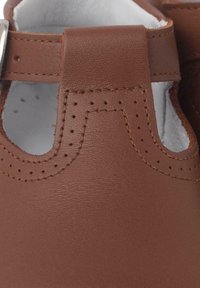 Zapato de cuero marrón con formas recortadas, detalles perforados a lo largo de los bordes y un forro interior suave. Cuenta con un cierre de hebilla de metal.