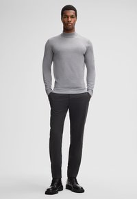 Gray fitted turtleneck sweater with long sleeves paired with dark trousers and black lace-up boots, creating a streamlined look.