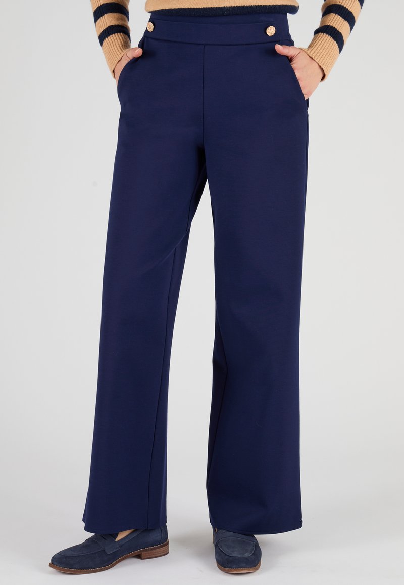 Navy-wijd been broek met een gladde textuur, voorzien van twee gouden knopen op de tailleband en zijzakken. Gepaard met navy instappers.