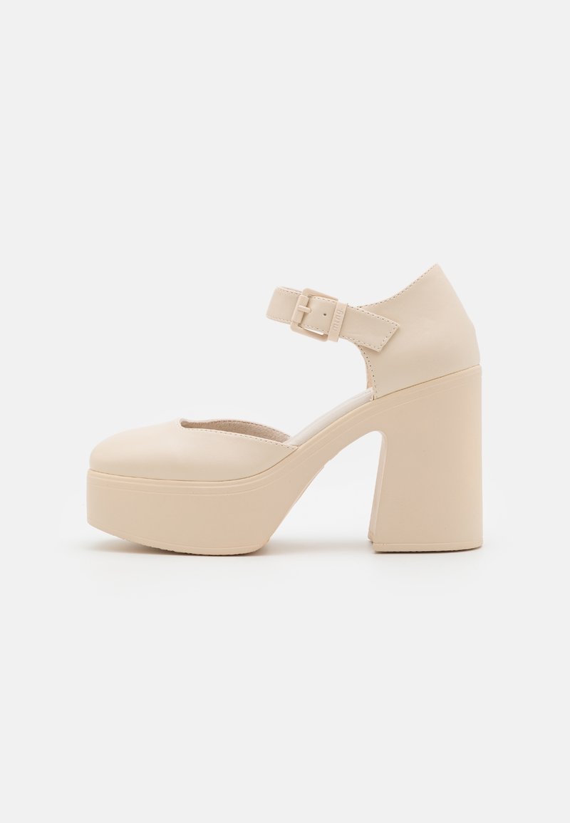Chaussure Mary Jane beige à plateforme avec talon haut épais et bride ajustable à la cheville avec boucle, vue de côté sur fond blanc.