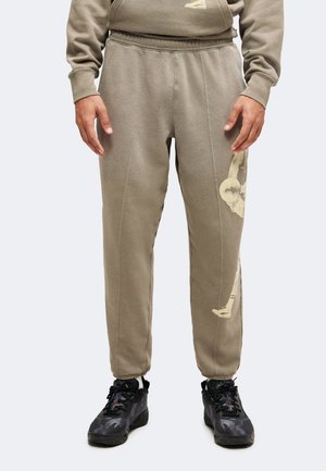 Personne portant un pantalon de jogging marron avec taille et poignets élastiques, des chaussures de sport noires et un sweat-shirt marron assorti.