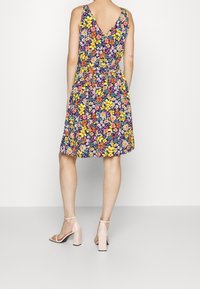 Květinové šaty s vypasovaným pasem, námořnické pozadí, živé žluté, růžové a zelené květy. Design s V-výstřihem, délka po kolena, spárováno s růžovými podpatky.