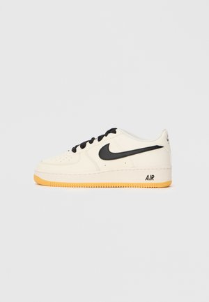Nike Air Force 1-sneakers i krämfärgad läder med svarta accenter och snören, med en texturerad gummisula och "AIR"-logotyp på hälen.