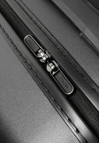 Zwarte rits met metalen hardware op een textuur zwart oppervlak, voorzien van een merkpull tab met het label "REDOLZ." Soepel, minimalistisch ontwerp.