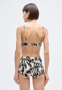 Conjunto de biquíni padrão preto e branco com um top tipo bandeau com alças finas e calções de cintura alta com acabamento em tecido texturizado.