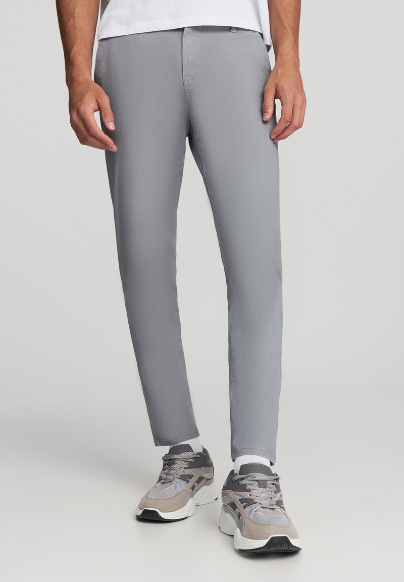 Szare slim-fit spodnie wykonane z gładkiego materiału, z ukrytym paskiem w talii i bocznymi kieszeniami, w połączeniu z szaro-beżowymi sneakersami.