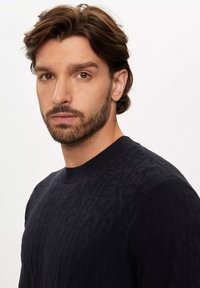 Maglione nero a maglia con un motivo testurizzato di lettere, scollatura rotonda e polsini a coste. Tessuto liscio con una leggera lucentezza.