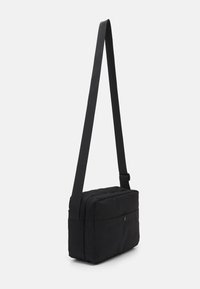 Black crossbody bag made of soft, textured fabric. Rectangular shape with zip closure, adjustable strap, and front snap pocket.