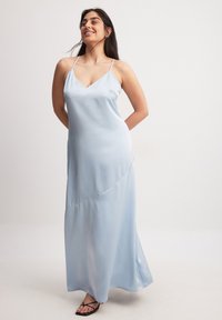Šviesiai mėlyna satino maksi suknelė su špagatinėmis petnešėlėmis ir V formos kaklo iškirpte. Įtaisyta subtili kreivė siūlų detalė; lygus paviršius, grindis siekiantis dizainas.