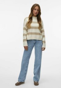 Pull rayé en crème et beige avec un col rond et des poignets côtelés, assorti à un jean large bleu clair et des chaussures marron.