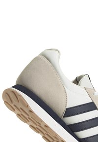 Zapatilla con tacón de ante beige, parte superior de tejido blanco y rayas en azul marino. La suela de goma presenta un patrón zigzag texturizado para un mejor agarre.