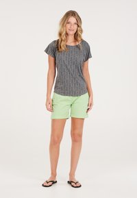 Grijze geblokte korte mouw top met een ronde hals, gecombineerd met lichtgroene opgerolde shorts en zwarte slippers.