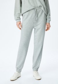Grijze sweatpants van zacht materiaal met een elastische tailleband en manchetten. Voorzien van een trekkoord en zijzakken. Gepaard met witte sneakers.