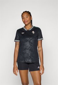 Maglietta sportiva nera con motivo floreale, scollo a V e strisce verdi sulle spalle. Presenta un logo sul petto sinistro. Vestibilità slim e maniche corte.