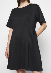 Vestido negro con escote redondo y mangas cortas. Presenta un corte holgado y bolsillos laterales, hecho de una tela suave y texturizada.