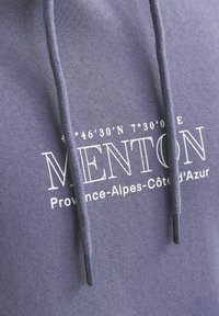 Sudadera gris con cordón trenzado, que presenta el texto impreso en blanco "MENTON Provincia-Alpes-Côte d'Azur" y coordenadas geográficas.