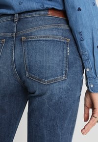 Džíny z denimu v středně modré barvě s texturovaným povrchem, které mají dvě zadní kapsy a jemné detaily šití.