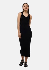 Robe débardeur en tricot côtelé noir avec une silhouette droite, atteignant le mollet. Associée à des sandales noires à lanières, au design minimaliste.