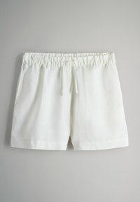 Shorts bianchi in lino con elastico in vita e cordino, esposti su uno sfondo grigio neutro.
