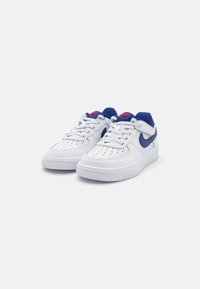 White leather sneakers with blue accents and red branding. Features perforated toe box and textured rubber outsole. Low-top design.