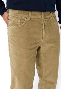 Pantaloni in corduroy marrone chiaro con righe verticali, dotati di tasche anteriori, chiusura con bottone in metallo e design classico a gamba dritta.