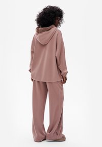 Overmaatse roze hoodie met een textuur en een bruin gevoerd capuchon, gecombineerd met bijpassende wijde broekspijpen, beide gemaakt van een zachte stof.