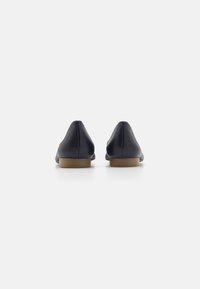 Balerini din piele neagră, cu vârf ascuțit și toc jos de culoare bej, având o textură fină și un design minimalist pe partea din spate.