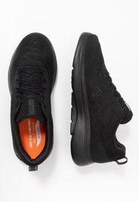 Scarpe sportive nere con tomaia in mesh traspirante, suola spessa e interno arancione. Presentano una chiusura con lacci e un manico per indossarle facilmente.