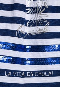 Navy ja valkoinen raidallinen kangas, jossa on metallinhohtoisia hopea kukkakuoseja, sinisiä paljettiraitoja ja teksti "LA VIDA ES CHULA!" alareunassa.