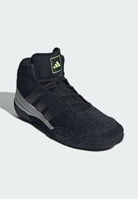 Black athletic shoe with mesh upper, padded collar, and three white stripes. Features a textured rubber outsole and a green logo patch.