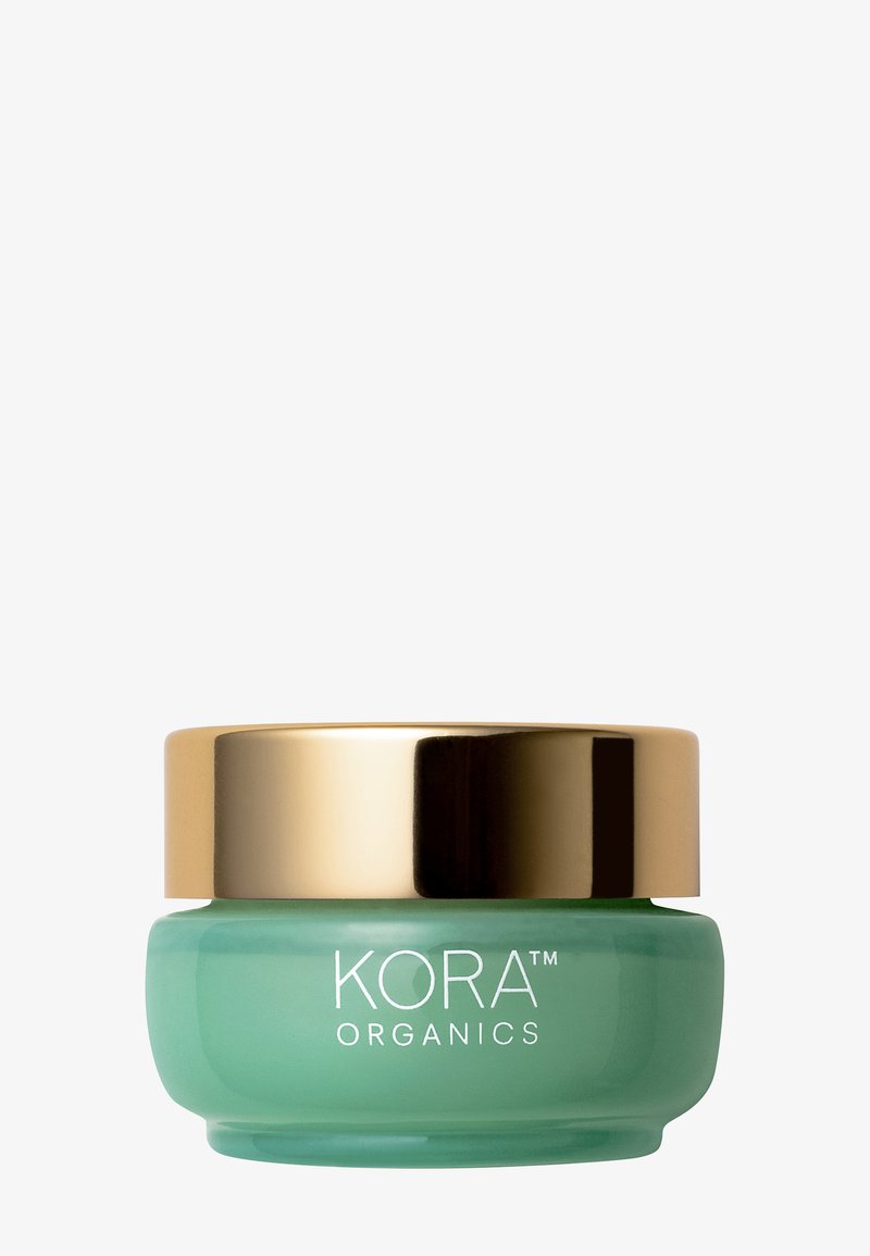 Bocal en verre vert avec un couvercle doré, portant le texte "KORA ORGANICS" en blanc sur le devant. Matériau lisse et translucide ; forme arrondie.