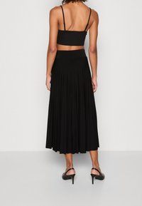 Top corto nero con spalline sottili abbinato a una lunga gonna nera plissettata. L'outfit presenta una texture liscia e una vita aderente.