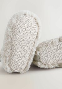 Jasne, miękkie kapcie z fakturowaną podeszwą o wzorzystym designie. Miękki materiał otacza krawędzie dla komfortu.