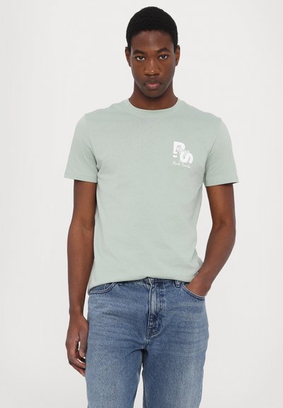Lys grønn t-skjorte med korte ermer i myk bomull, med et hvitt grafisk trykk på venstre bryst. Brukt sammen med blå denim jeans.
