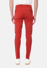 Pantaloni di cotone rossi con vestibilità slim, dotati di due tasche posteriori e una texture liscia. Abbinati a sneakers bianche.