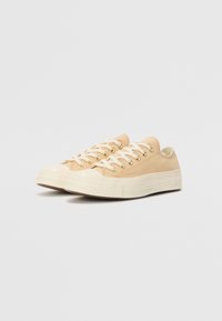 Beiga canvas sneakers med krämfärgade gummisulor, rund tå och vita snören. Har ögla i guldton och en strukturerad sidopanel.