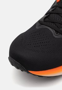 Black athletic shoe featuring a textured knit upper, orange accents along the sole, and a rounded toe for a sleek design.