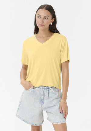 Žuta v-neck majica od mekog materijala, kratkih rukava, opuštenog kroja. Uparena sa svijetloplavim trapericama. Jednostavan i ležeran dizajn.