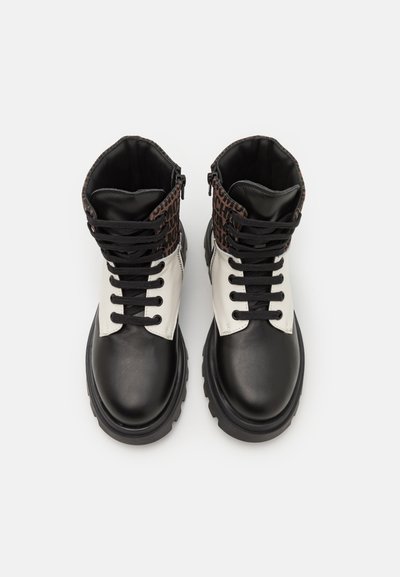 Bottines à lacets noires et blanches avec un col en motif brun, dotées d'une semelle en caoutchouc épaisse et de détails de couture visibles.