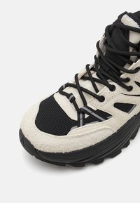 Strukturierter schwarzer und cremefarbener Wanderschuh mit gepolsterter Knöchelunterstützung, Mesh-Einsätzen und schwarzen Schnürsenkeln. Dicke Laufsohle für Traktion und Unterstützung.